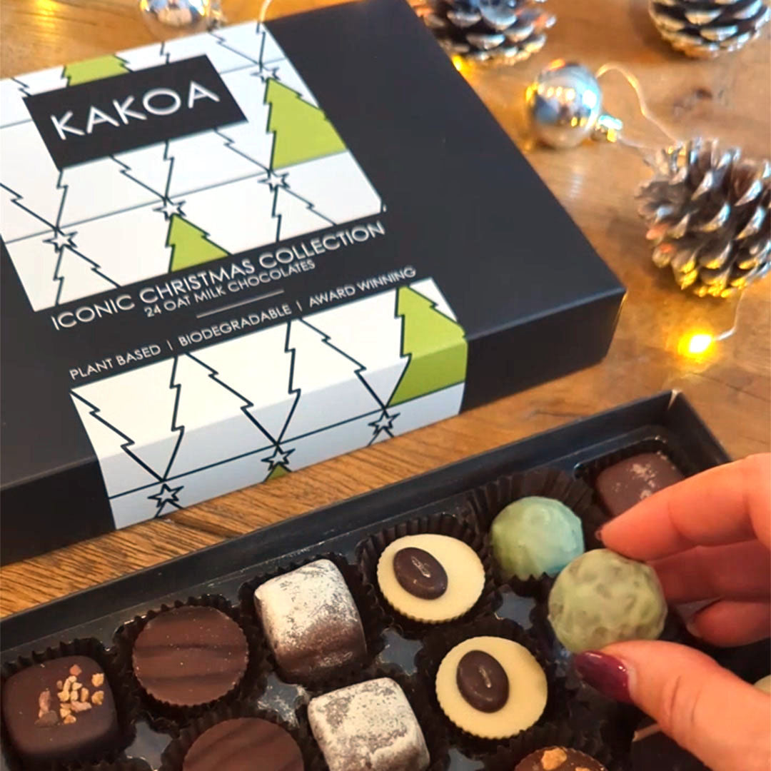 Kakoa Iconic Christmas Collection chocolate box on a wooden surface with a hand reaching for a chocolate.